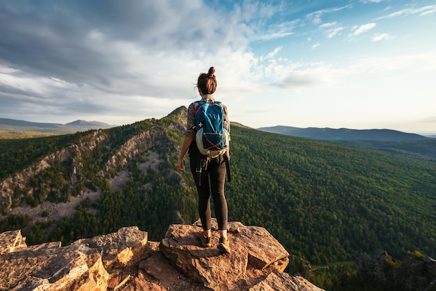 Una giovane turista con uno zaino si gode il tramonto dalla cima della montagna. Un viaggiatore sullo sfondo delle montagne. Un turista con uno zaino è in piedi sulla cima della montagna