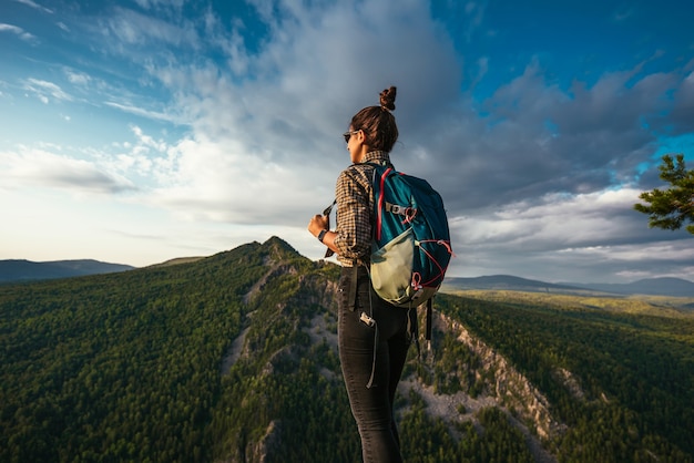 Una giovane turista con uno zaino si gode il tramonto dalla cima della montagna. Un viaggiatore sullo sfondo delle montagne. Un turista con uno zaino è in piedi sulla cima della montagna