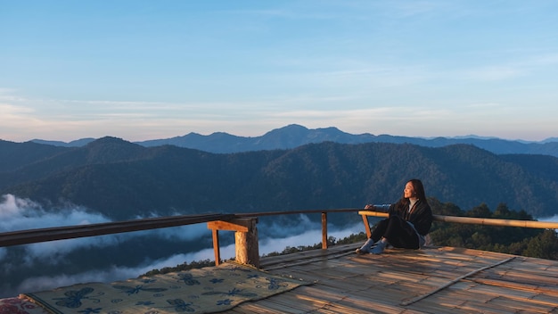 Una giovane viaggiatrice seduta sul balcone di legno guardando una bellissima montagna e un mare di nebbia