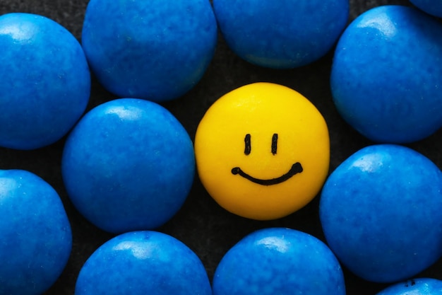 Una goccia gialla con faccia felice dipinta tra quelle blu Differenza e concetto di unicità