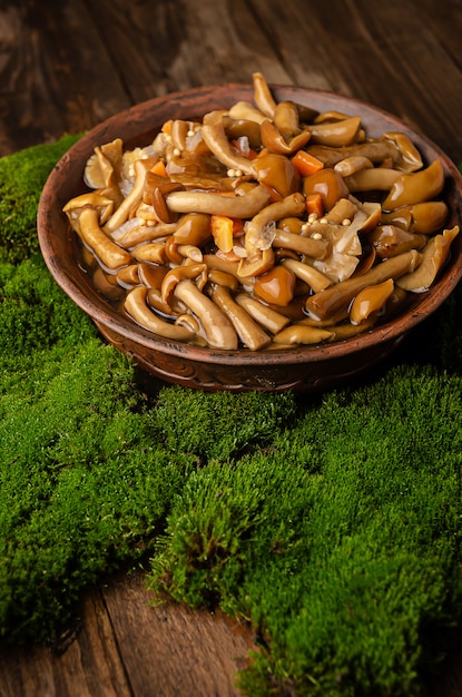 Una grande ciotola di argilla con funghi selvatici (funghi di miele), si trova su un vecchio tavolo di legno con muschio verde. Prodotti ecologici, raccolta naturale