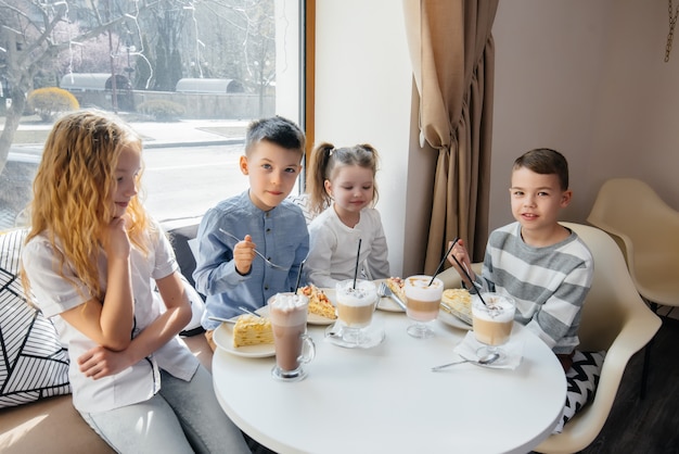 Una grande compagnia amichevole di bambini celebra la vacanza in un caffè con un delizioso dessert.