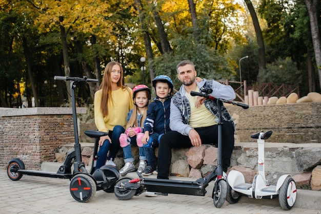 Una grande famiglia felice guida Segway e scooter elettrici nel parco in una calda giornata autunnale durante il tramonto. Vacanza in famiglia nel Parco.