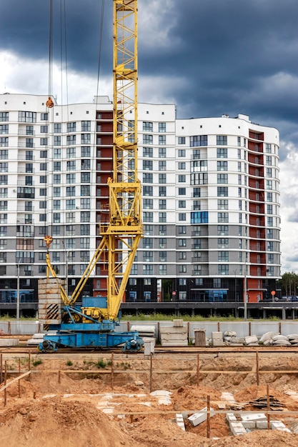 Una grande gru a torre in un cantiere edile sullo sfondo di una moderna casa monolitica Costruzione di alloggi moderni ingegneria industriale Costruzione di alloggi ipotecari