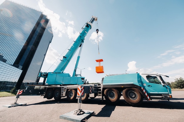 Una grande gru blu per camion è pronta per il funzionamento in un sito vicino a un grande edificio moderno. La più grande gru per autocarro con culla gialla per risolvere compiti complessi.