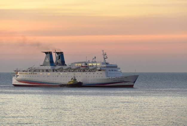 Una grande nave va in mare all'alba, cielo rosa e oro, vicino al rimorchiatore. Russia, Crimea, 2019