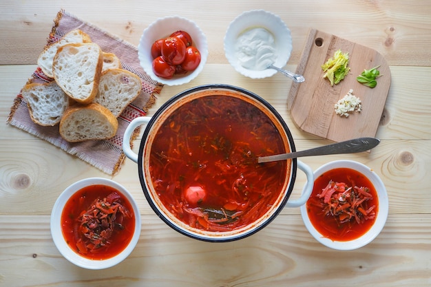 Una grande pentola con un borscht rosso su un tavolo di legno grezzo.