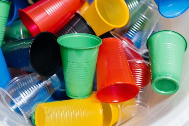 Una grande pila di bicchieri di plastica multicolori sparsi sul pavimento. Inquinamento ambientale da rifiuti umani.