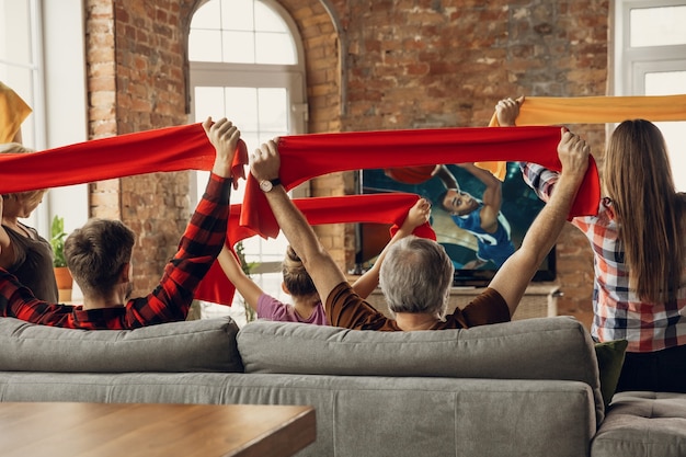 Una grande squadra familiare eccitata e felice guarda la partita sportiva insieme sul divano di casa