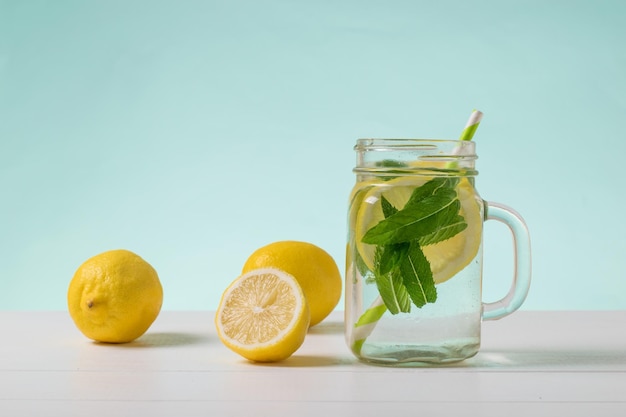 Una grande tazza di acqua fredda con limone e menta su un tavolo bianco su sfondo blu