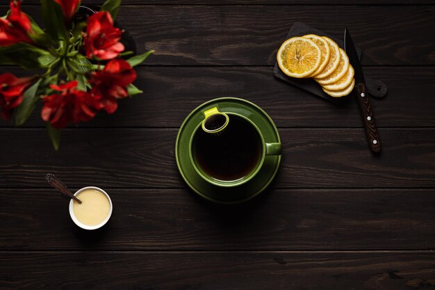 Una grande tazza di tè caldo affettato limone miele coltello e fiori su sfondo di legno colpo dall'alto