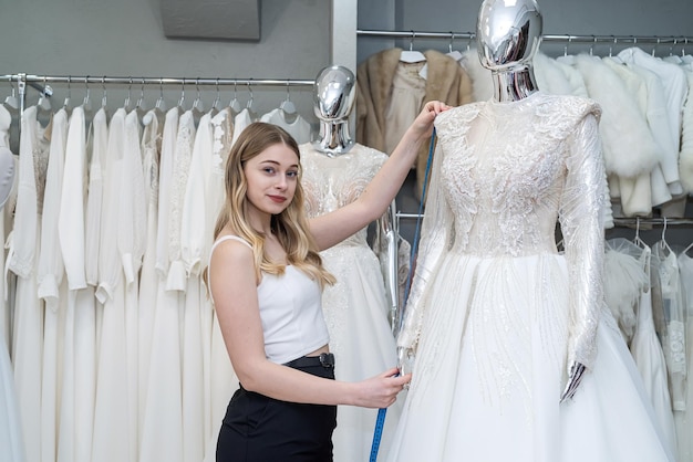 Una graziosa consulente di vendita misura un abito da sposa per un cliente e mostra una qualità impeccabile