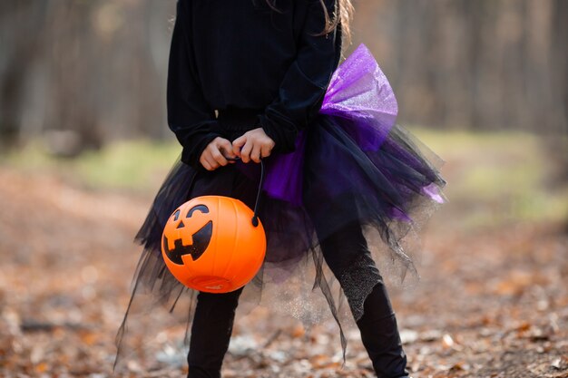 una graziosa ragazzina bruna con un costume da strega di Halloween tiene in mano un cesto di zucca