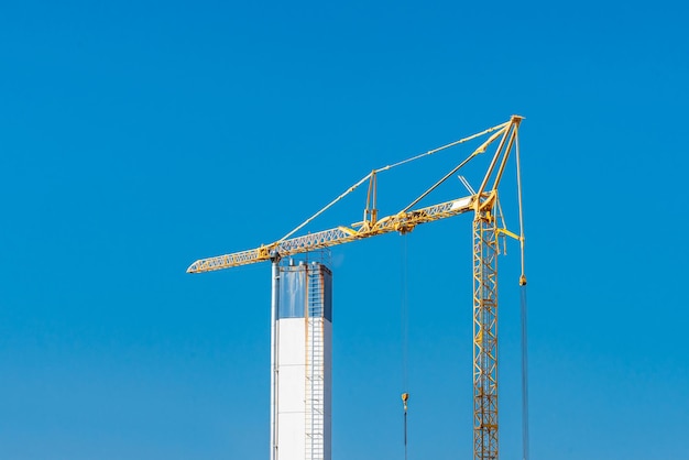 Una gru a torre gialla tendeva una freccia sopra una torre rettangolare contro un cielo blu