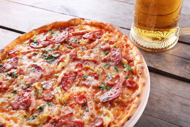 Una gustosa pizza e un bicchiere di birra sono sul tavolo di legno da vicino