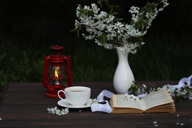 Una lanterna rossa con un vaso bianco di fiori accanto a una tazza di caffè e un libro sopra
