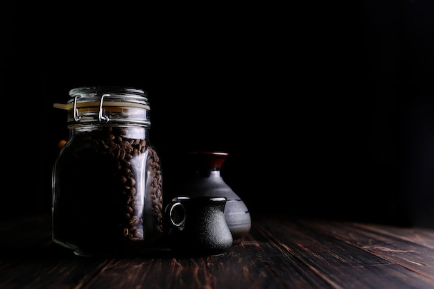 Una lattina di caffè, una tazza e un turk su un tavolo di legno, su uno sfondo nero.