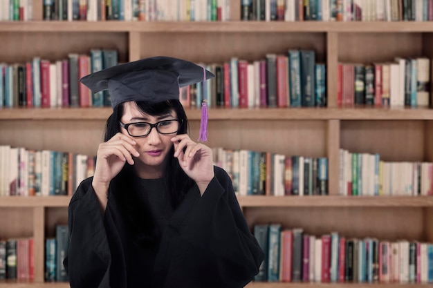 Una laureata asiatica che piange in biblioteca.
