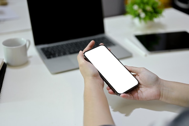 Una lavoratrice d'ufficio che utilizza il suo smartphone al mockup dello schermo bianco del telefono da scrivania