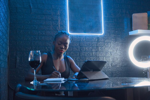 Una lavoratrice nera che scrive su un taccuino e utilizza un tablet digitale in un pub