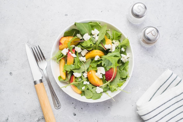 Una leggera insalata estiva di pesche rucolla e formaggio su fondo grigio chiaro