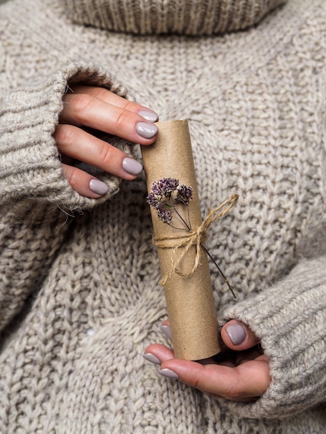 Una lettera decorata con un fiore di origano nelle mani di una ragazza. una ragazza con un maglione di lana tiene una lettera fatta di carta Kraft. Atmosfera pre-festiva