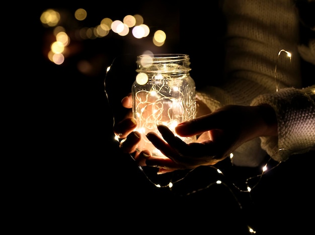 Una luce nelle mani di un uomo una foto di un barattolo con una ghirlanda e un bokeh dalle luci