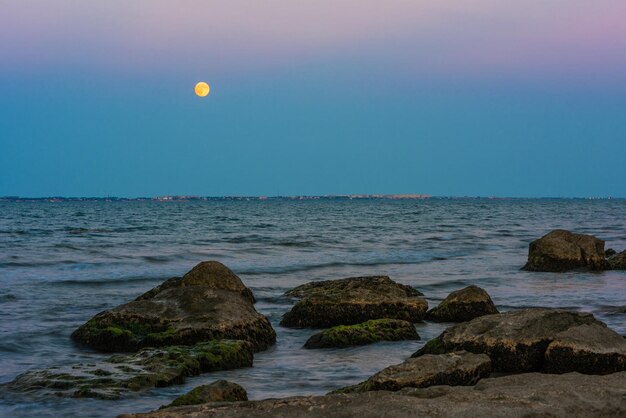 Una luna piena sorge sull'acqua in spiaggia.