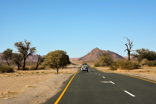 Una lunga strada asfaltata nel deserto in prospettiva contro un cielo blu Una jeep guida in lontananza