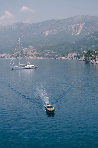 Una lussuosa barca a motore sportiva in legno trasporta i VIP da una grande barca bianca attraccata al largo della costa di