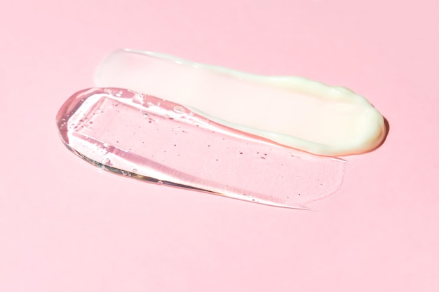 Una macchia di crema bianca e gel trasparente su sfondo rosa Prodotto cosmetico per la cura della pelle
