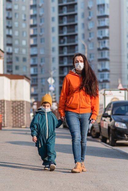 Una madre con un bambino in maschera medica cammina per strada durante la pandemia di coronavirus e Covid -19.