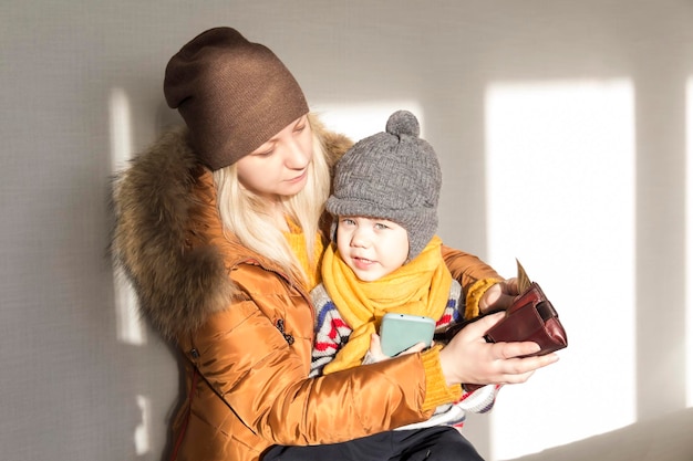 Una madre con un bambino piccolo in braccio è vestita calorosamente con capispalla che contano i soldi nella borsa Il concetto di crisi economica e grandi bollette nelle case