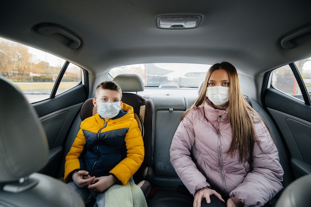 Una madre con un bambino sul sedile posteriore di un'auto in maschera che va in ospedale. Epidemia, quarantena.