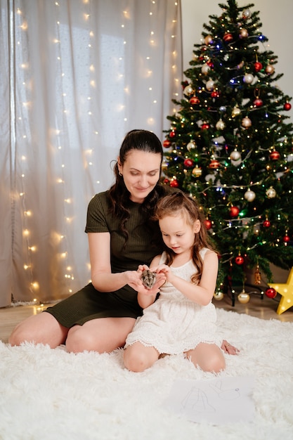 Una madre con una figlia piccola che gioca con un criceto all'albero di natale