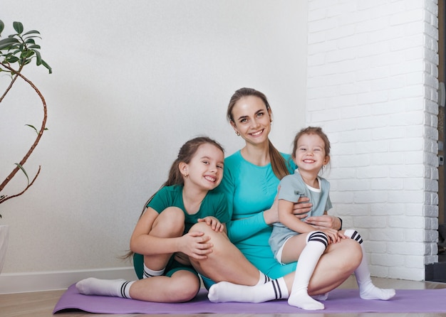 Una madre e le sue figlie sono sedute sul pavimento in divise sportive