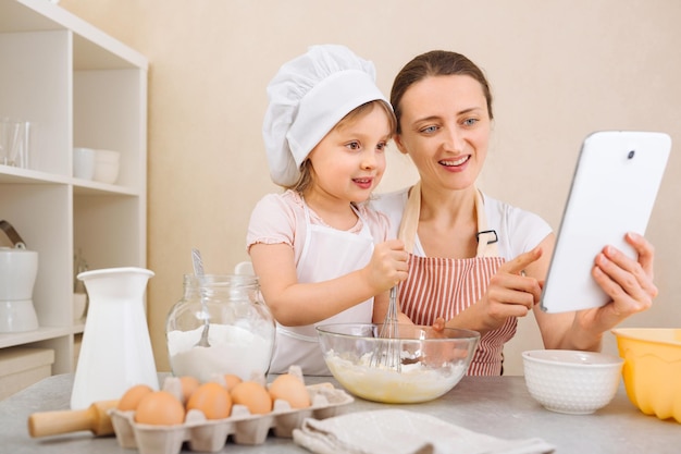 Una madre e sua figlia preparano insieme una torta e seguono una ricetta passo passo su una tavoletta