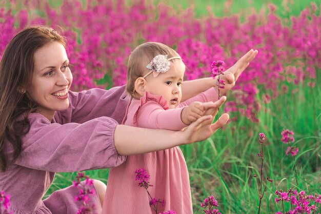 Una madre felice con una figlia bambina di due anni si diverte in un prato con fiori che sbocciano viola