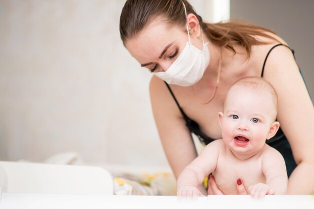 Una madre in una maschera protettiva con un bambino è seduta a casa