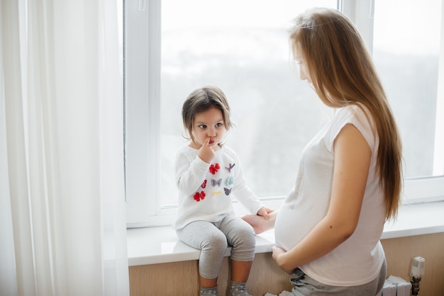 Una madre incinta è in piedi vicino alla finestra con la sua piccola figlia