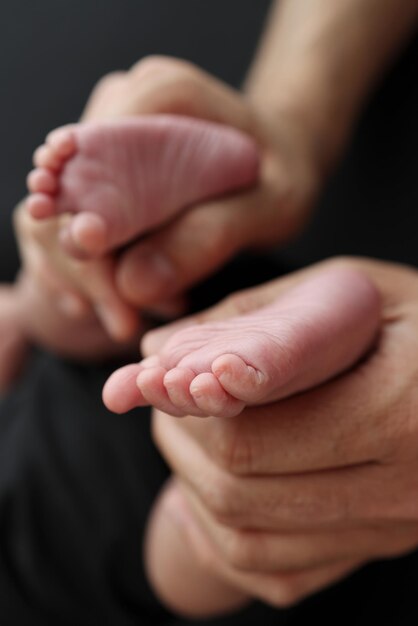 Una madre tiene i piedi di un neonato in una coperta nera su sfondo nero I piedi di un neonato nelle mani dei genitori Studio foto macro gambe dita piedi e talloni di un neonato