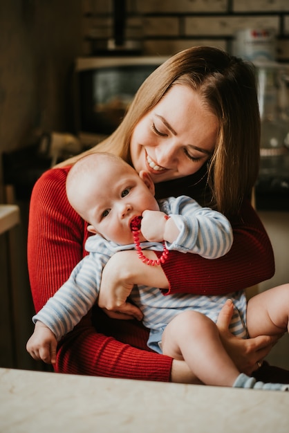 Una madre tiene in braccio un bambino. La mamma abbraccia il suo bambino. La ragazza si diverte e gioisce con il bambino. Una donna stringe un bambino.