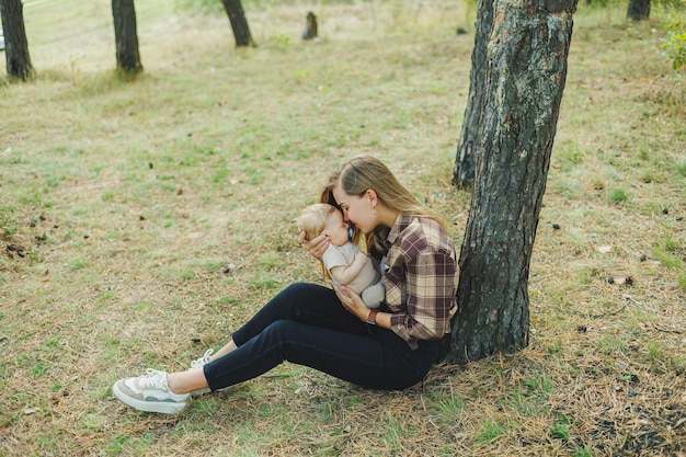 Una mamma carina è seduta nel parco sull'erba con un bambino piccolo tra le braccia una passeggiata con un bambino bambino in natura