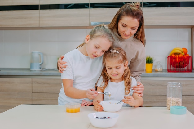 Una mamma e le sue due figlie aggiungono il miele alla farina d'avena in cucina.