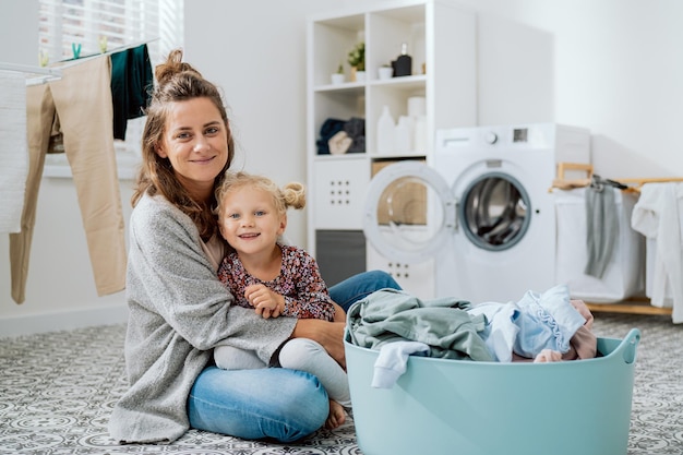 Una mamma si siede sul pavimento della lavanderia con la sua giovane figlia