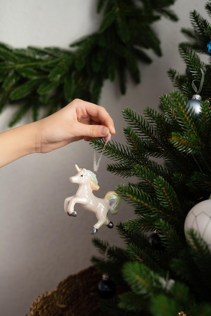 Una mano appende un giocattolo di unicorno su un albero di Natale artificiale