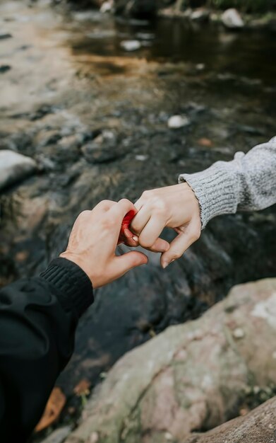 Una mano che afferra un'altra mano con un fiume come sfondo usando un concetto d'amore di anello di gomma