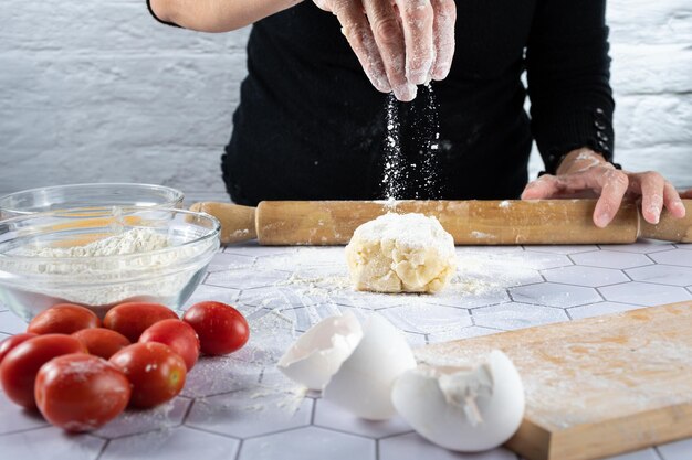 Una mano che getta la farina in un impasto tra ingredienti e strumenti da cucina