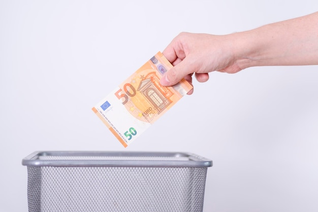 Una mano che mette le banconote in euro in un bidone della spazzatura