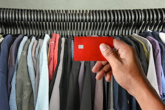 Una mano che tiene la carta di credito su t-shirt rack in negozio, concetto di shopping di vita moderna